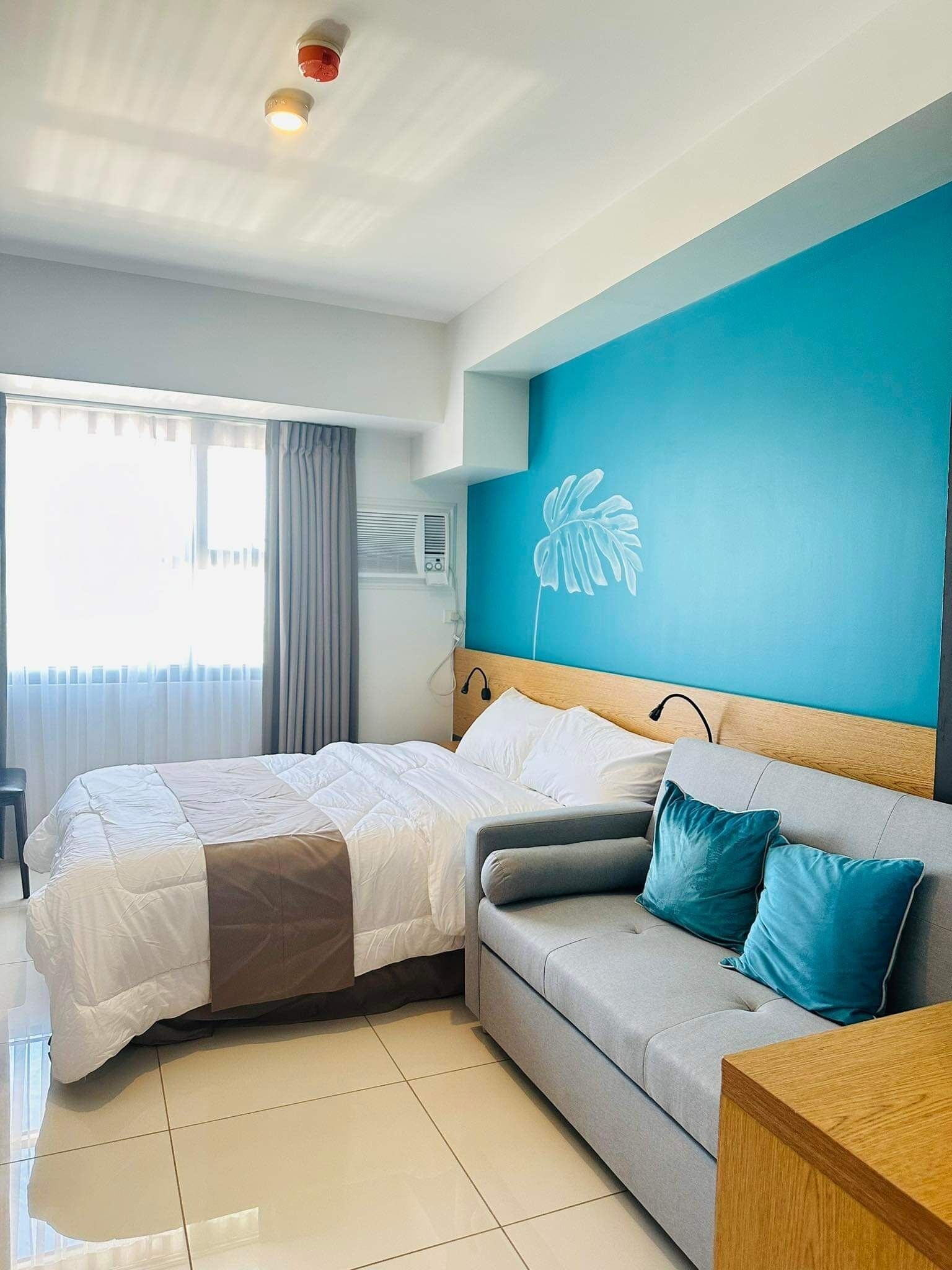 Een moderne hotelkamer met een bed, een grijze bank en een blauwe accentmuur.