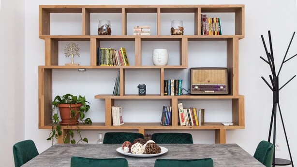 Un coin repas avec une bibliothèque en bois, une table sur laquelle se trouve une assiette de nourriture et des chaises vertes.