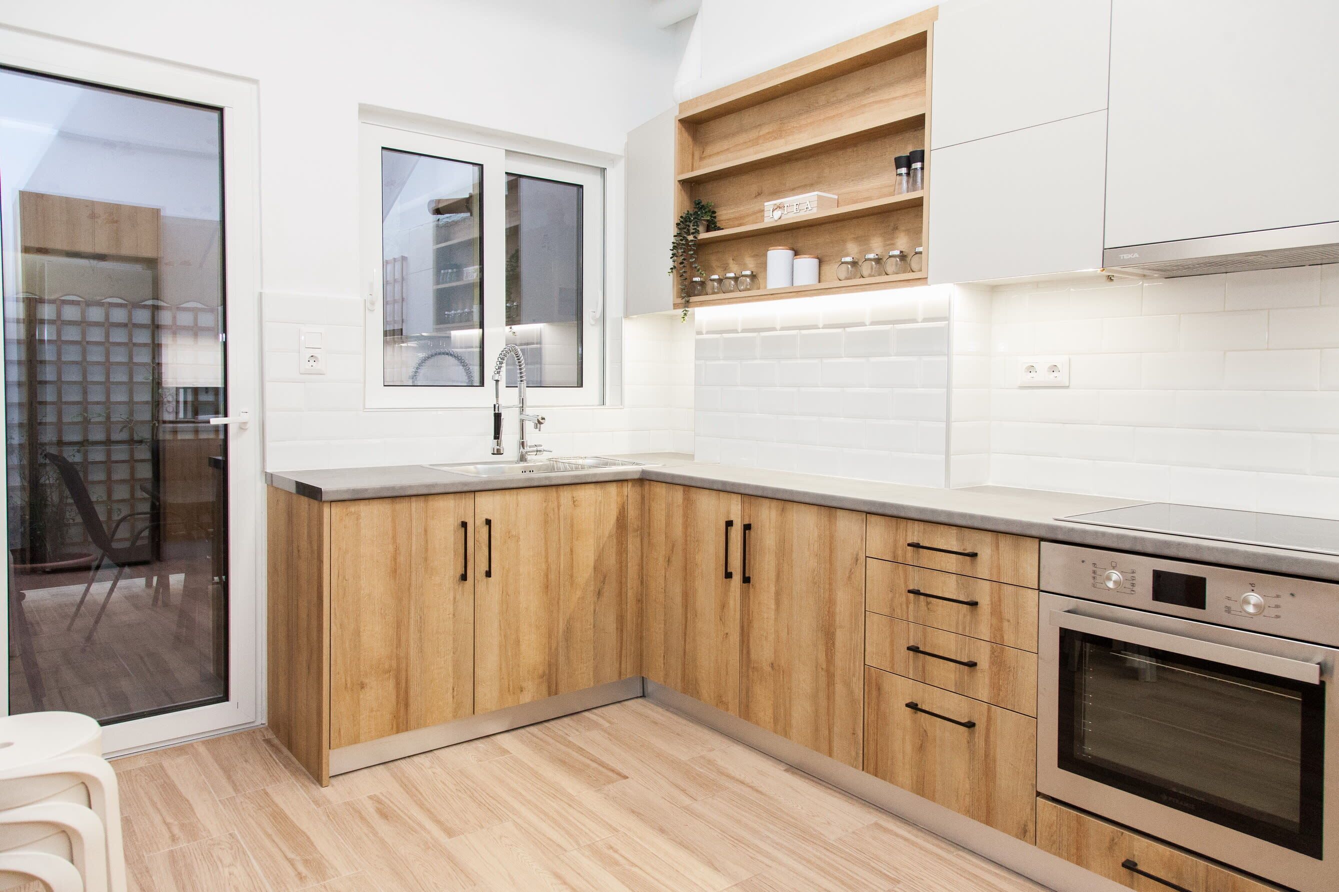 Een moderne keuken met houten kastjes, een inbouwoven en een raam boven de spoelbak.