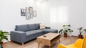 Un salon moderne avec un canapé gris, une table basse en bois et un fauteuil jaune. On y trouve des plantes en pot et des tableaux encadrés accrochés au mur.