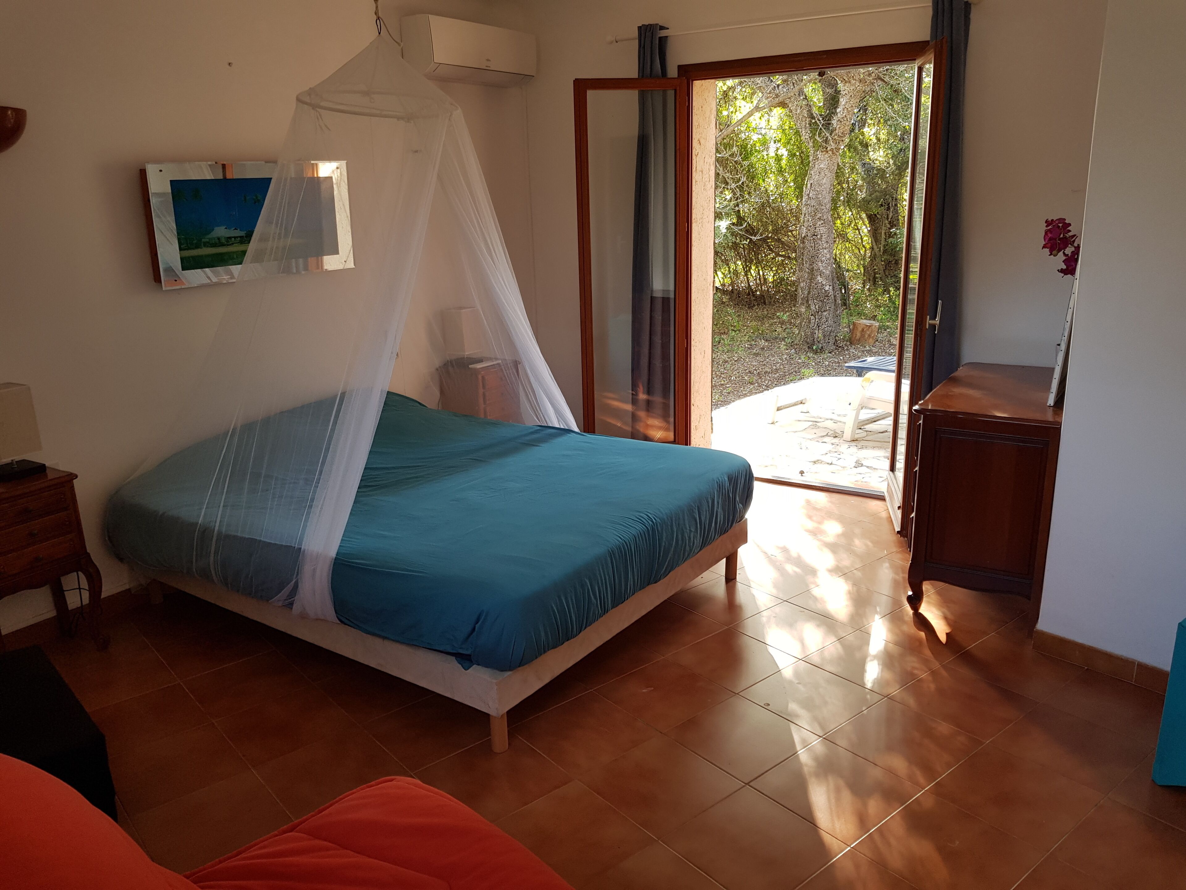Un dormitorio con cama, una mesita de noche, una ventana con vistas a árboles y un ventanal corredero que da a un área exterior.