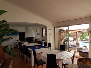 Uma sala de jantar com mesa de bilhar, cadeiras e uma mesa com toalha de mesa florida.