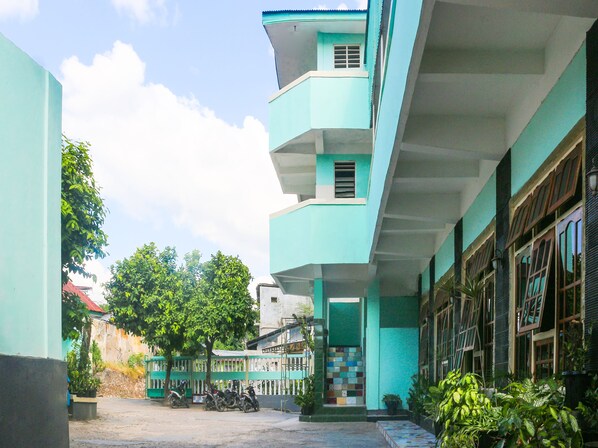 Um edifício de vários andares com fachada azul clara, entrada gradeada e escadaria que leva aos andares superiores.