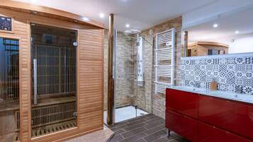 Bathroom features a shower with a glass door and handheld showerhead, a vanity with a tiled backsplash, and dark tile flooring.