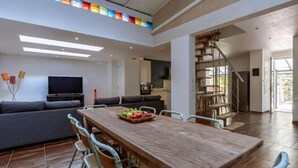 A spacious living area with a wooden dining table, a sofa, and a TV. - Lou Roucas : Pleasant village house with view (Fontaine-de-Vaucluse)