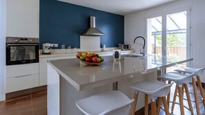 A modern kitchen with a central island, white bar stools, and a blue accent wall. - Lou Roucas : Pleasant village house with view (Fontaine-de-Vaucluse)