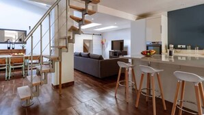 A modern kitchen with a central island, wooden staircase, and a dining area with bar stools. - Lou Roucas : Pleasant village house with view (Fontaine-de-Vaucluse)