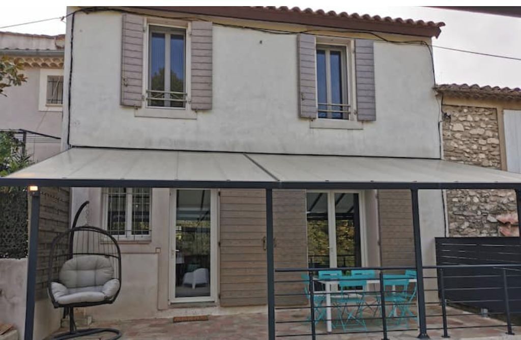 Une maison à deux étages dotée d’un patio couvert, d’un fauteuil suspendu et d’un espace salon extérieur.
