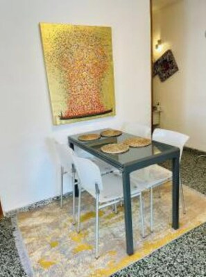 A dining area with a table and chairs, a rug, and a wall with a colorful painting.