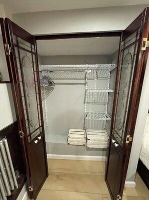 Walk-in closet with a traditional design, featuring a door with glass panels and a brass handle, metal shelving units, and a tiled floor.