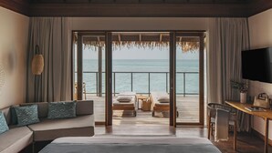 A bedroom with a large bed, a sofa, a TV, a desk, and a view of the sea. - Meliá Whale Lagoon Maldives (Bodufinolhu Island)