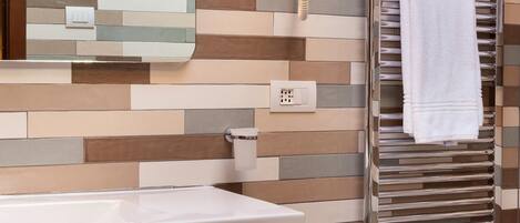 A bathroom with a modern sink, a towel rack with a white towel, and a mirror with a mosaic tile backsplash.