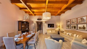 A dining area with a wooden table set for six, flanked by two sofas and a coffee table. A bookshelf and a television are visible in the background. - Maison De Charme in Sorrento (Sorrento)