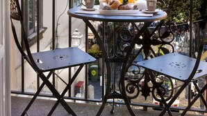 Un balcón con una mesa dispuesta para el desayuno, incluyendo tazas y una tetera, con vistas a una zona residencial con edificios y vegetación.