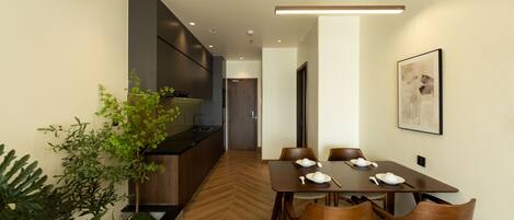 A modern dining area with a wooden herringbone floor, a long table with six chairs, and a kitchen area with a built-in stove and cabinets.