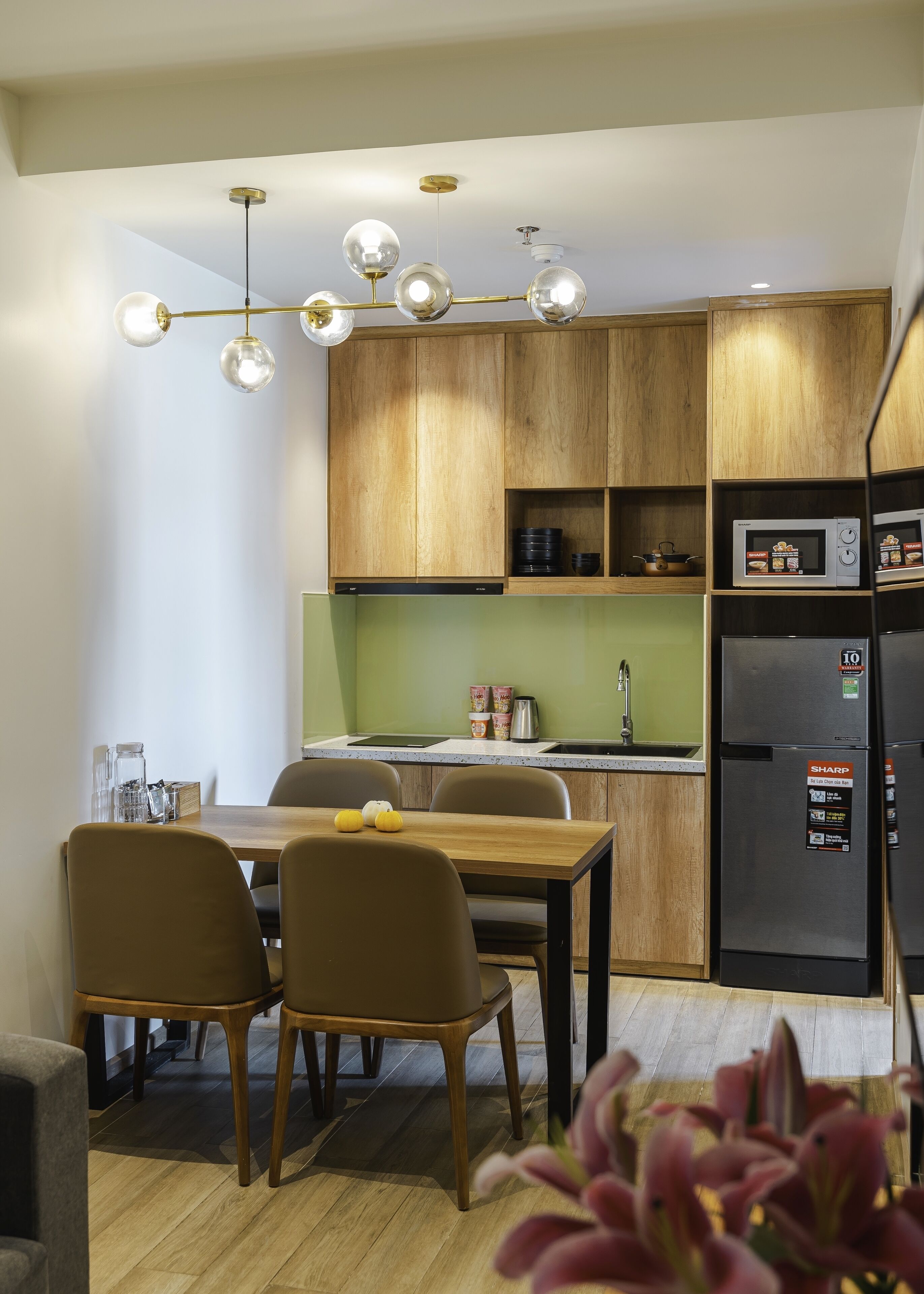 A modern kitchen with wooden cabinets, a stainless steel refrigerator, and a dining area with a table and chairs.