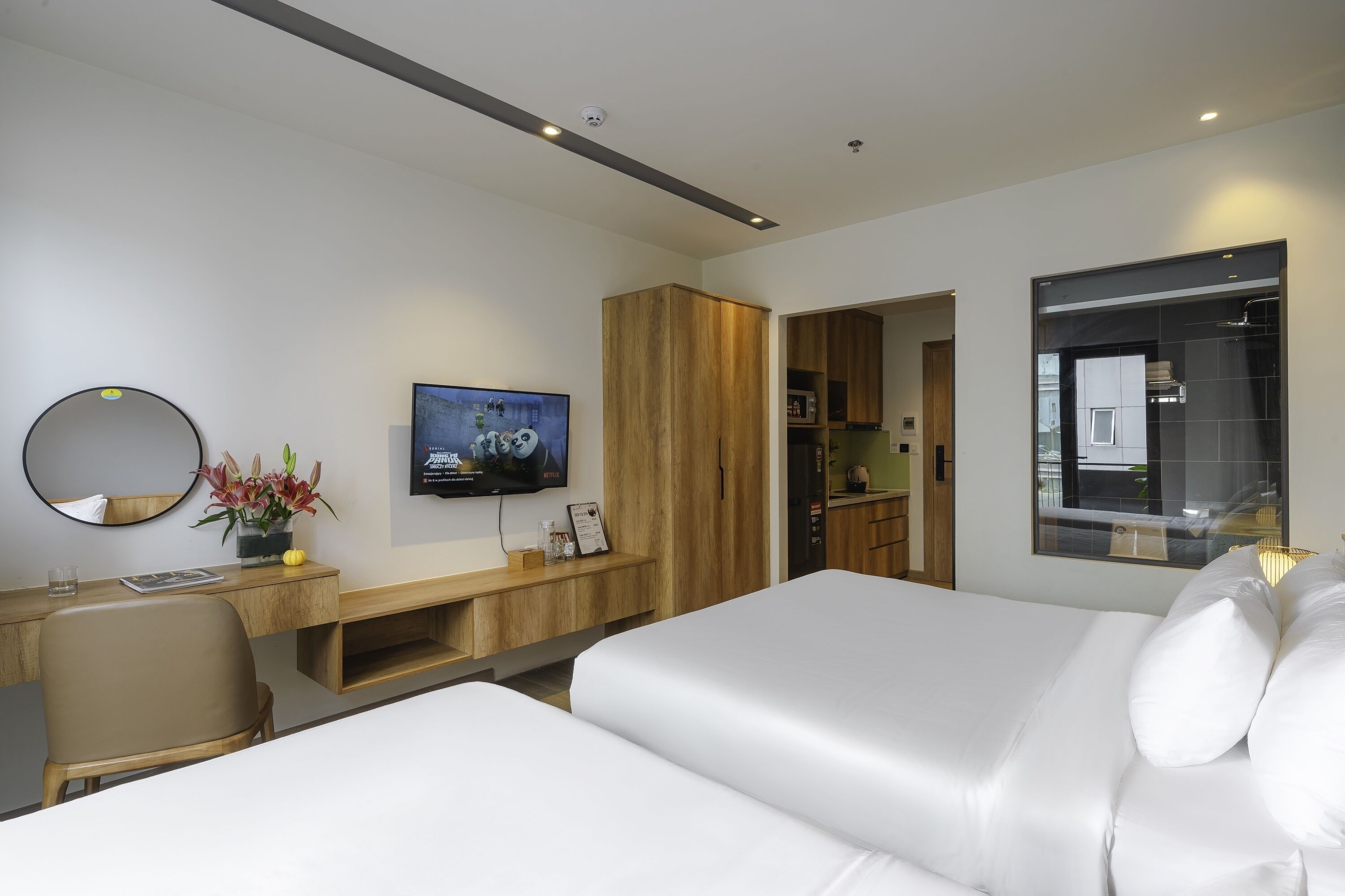 Een moderne hotelkamer met een bed, een bureau met een computer, een televisie en een houten garderobe.