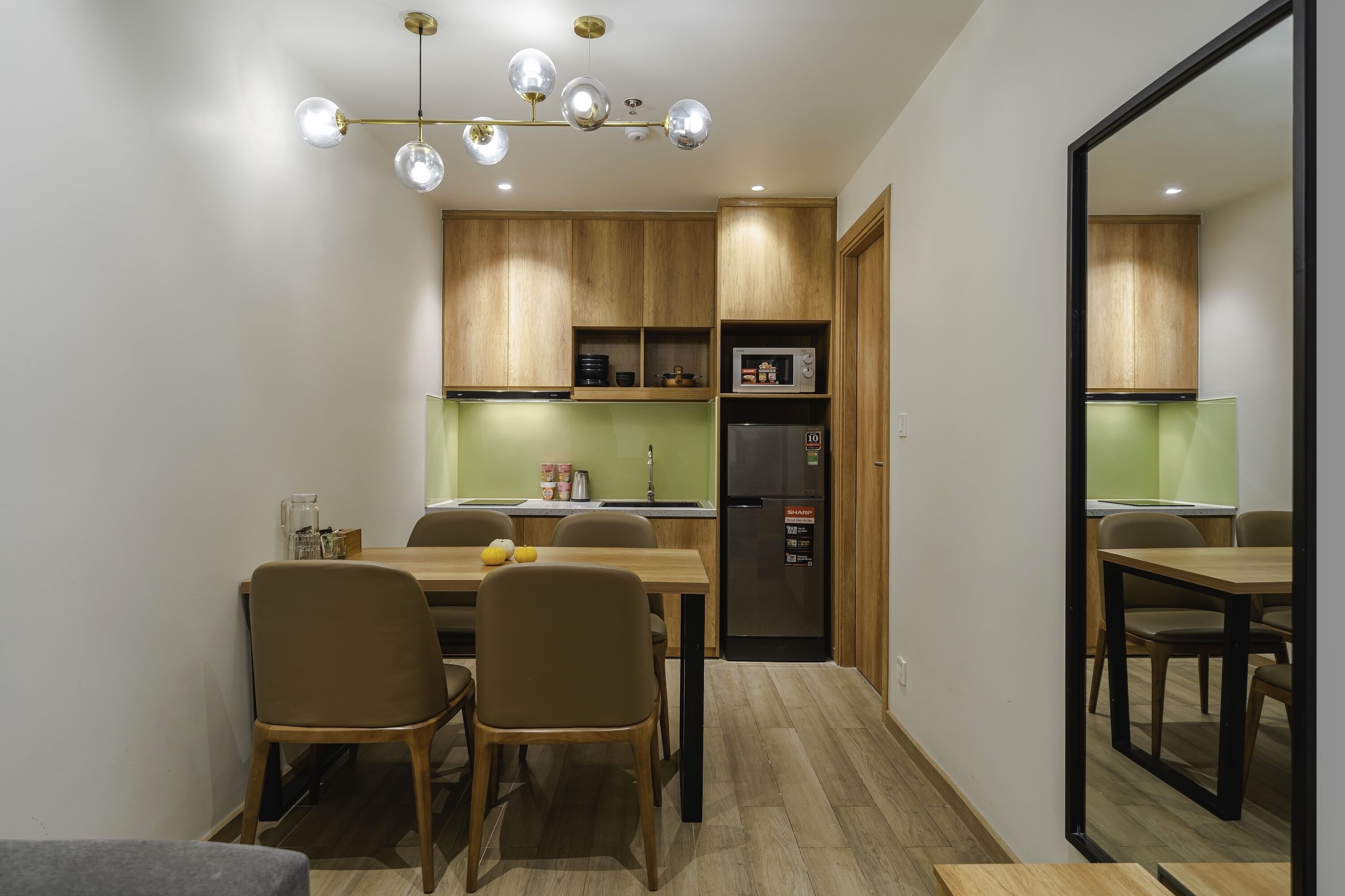 A compact kitchen with wooden cabinets, a black refrigerator, and a dining area with chairs and a table.