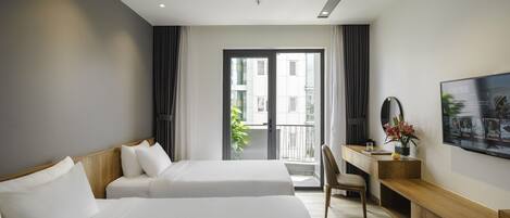 A hotel room with two beds, a desk, a chair, a TV, and a balcony with a view of buildings.