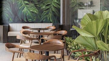 Een restaurantinterieur met houten stoelen, een muurschildering van groene bladeren en hangende pendellampen.