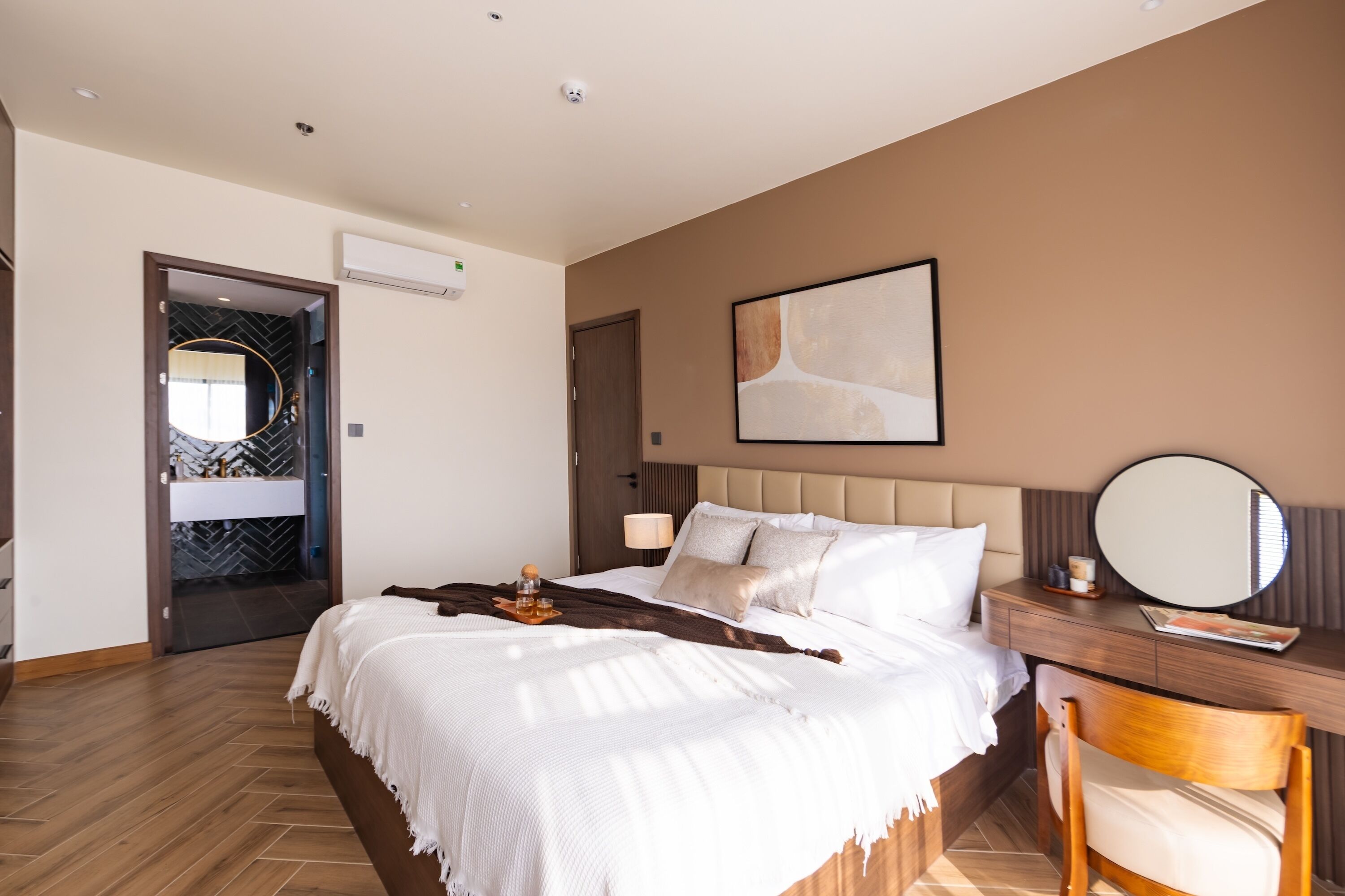 Habitación de hotel moderna con una cama grande, un escritorio con una silla, un espejo redondo y un cuadro en la pared.