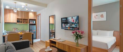 A modern hotel room with a sofa, a small table, a TV mounted on the wall, and a bed.