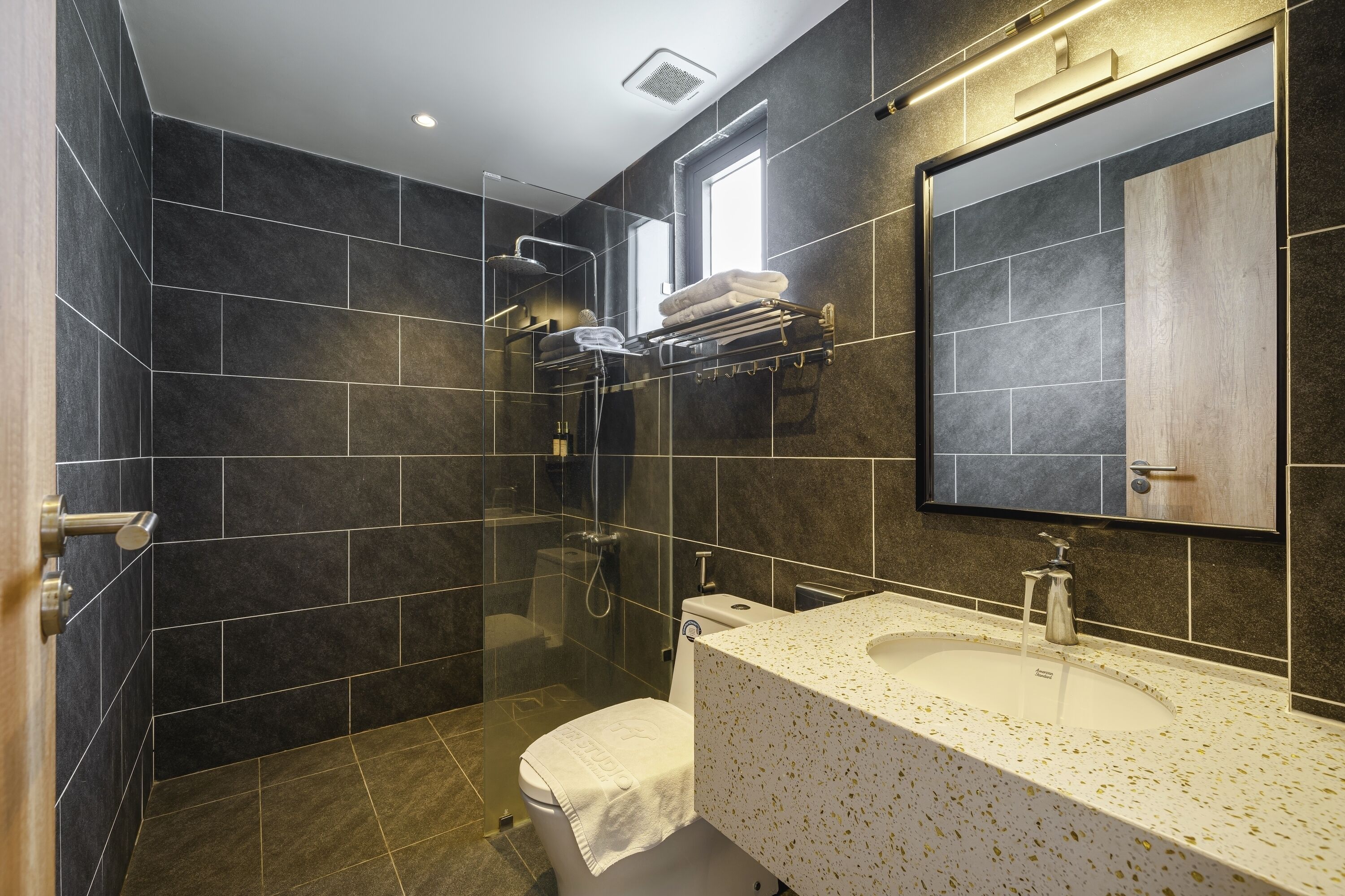 A modern bathroom with dark tiles, a glass-enclosed shower, a white sink, and a mirror above the sink.