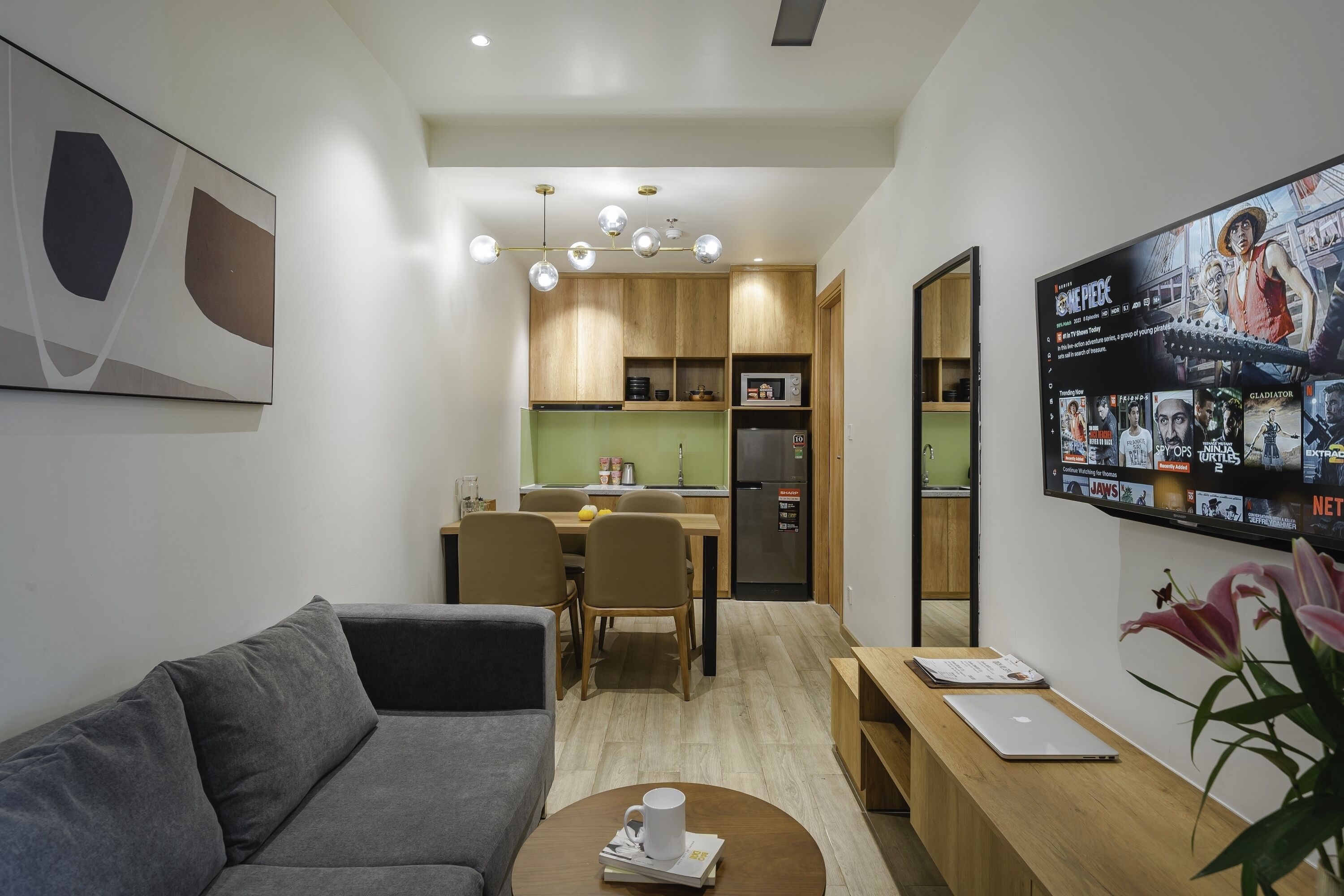 Un salón moderno con un sofá gris, una mesa de centro de madera y un televisor en la pared que muestra un póster de película.