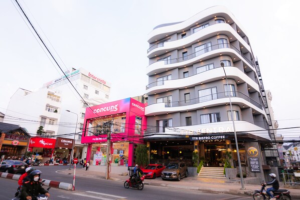 Un edificio de varios pisos con fachada curva, una cafetería en la planta baja y diversos comercios a nivel de calle.