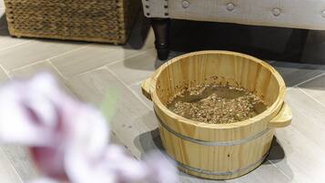 A wooden bucket on a tiled floor with a wicker basket and a cushioned chair in the background.