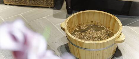 A wooden bucket on a tiled floor with a wicker basket and a cushioned chair in the background.