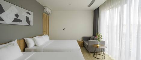 Une chambre d’hôtel moderne avec deux lits, un canapé, une petite table et une grande fenêtre agrémentée de rideaux légers.