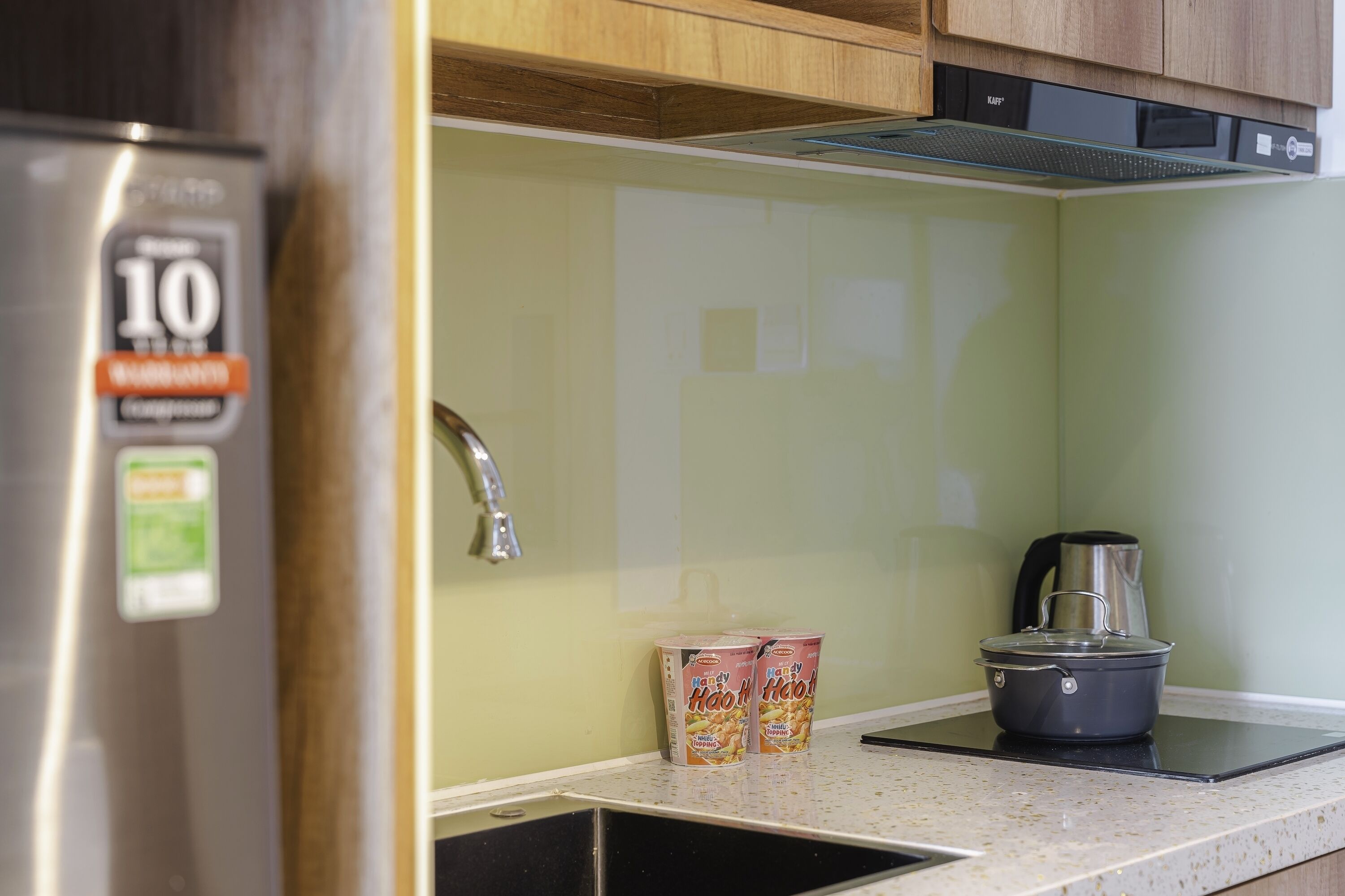 Una cocina con un refrigerador de acero inoxidable, una tetera y dos latas de Milo sobre la encimera.