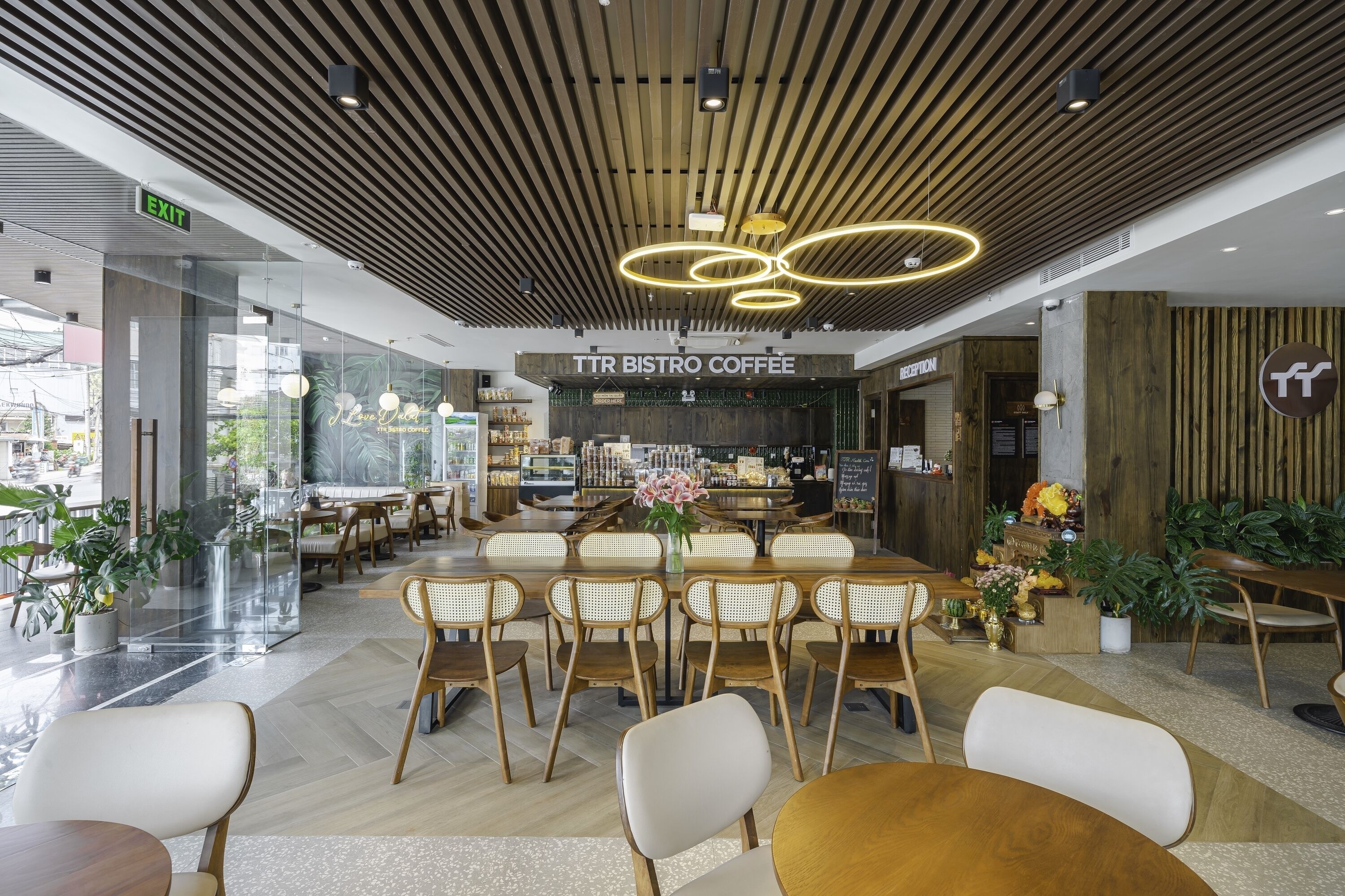 Un café-bistro moderne avec un plafond en bois, des cloisons en verre et différents types de sièges, notamment des tables et des chaises.