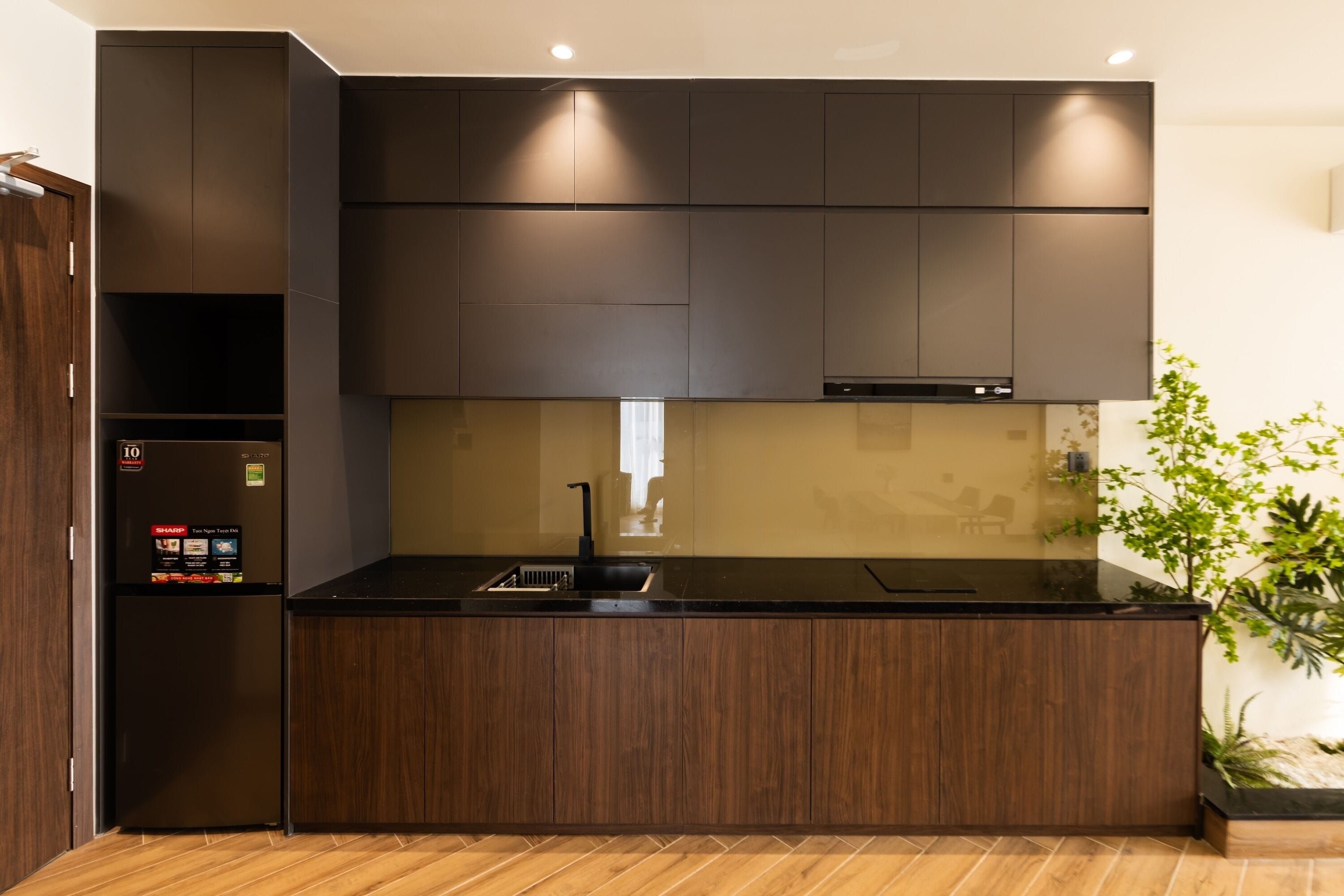A modern kitchen with dark cabinetry, a built-in oven, and a black countertop.