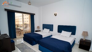 Ein Hotelzimmer mit zwei Betten, einem Schreibtisch, einem Stuhl und Blick auf ein Gebäude durch das Fenster.