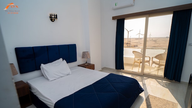 Ein Schlafzimmer mit Bett, Nachttisch, Lampe und Blick auf den Strand mit Windkraftanlagen.