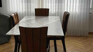 Un coin repas comprenant une table rectangulaire et six chaises, un canapé et une grande fenêtre ornée de rideaux légers.