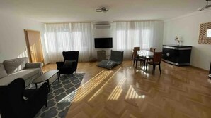 Un salon spacieux comprenant un canapé, des fauteuils, une table basse, une table à manger avec des chaises, un téléviseur et un meuble décoratif.