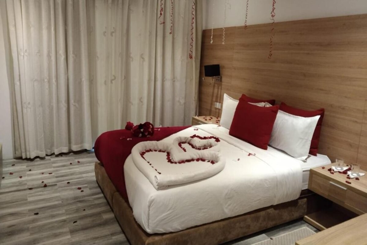 Una cama bien hecha con un arreglo de pétalos de rosa formando un corazón sobre la colcha.