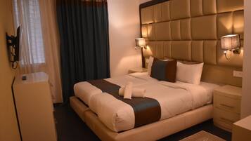 Una habitación de hotel con una cama grande, dos mesitas de noche, un armario y una ventana con cortinas.