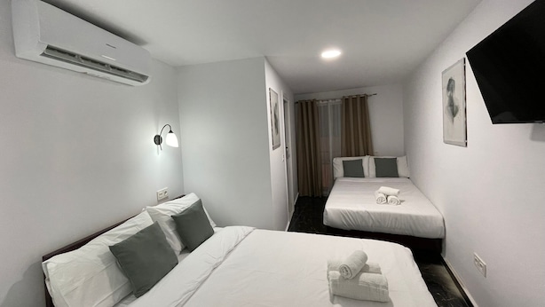 A hotel room with two beds, a flat-screen TV, an air conditioner, and a wall-mounted light fixture. - SL Hostel Marbella (Marbella)