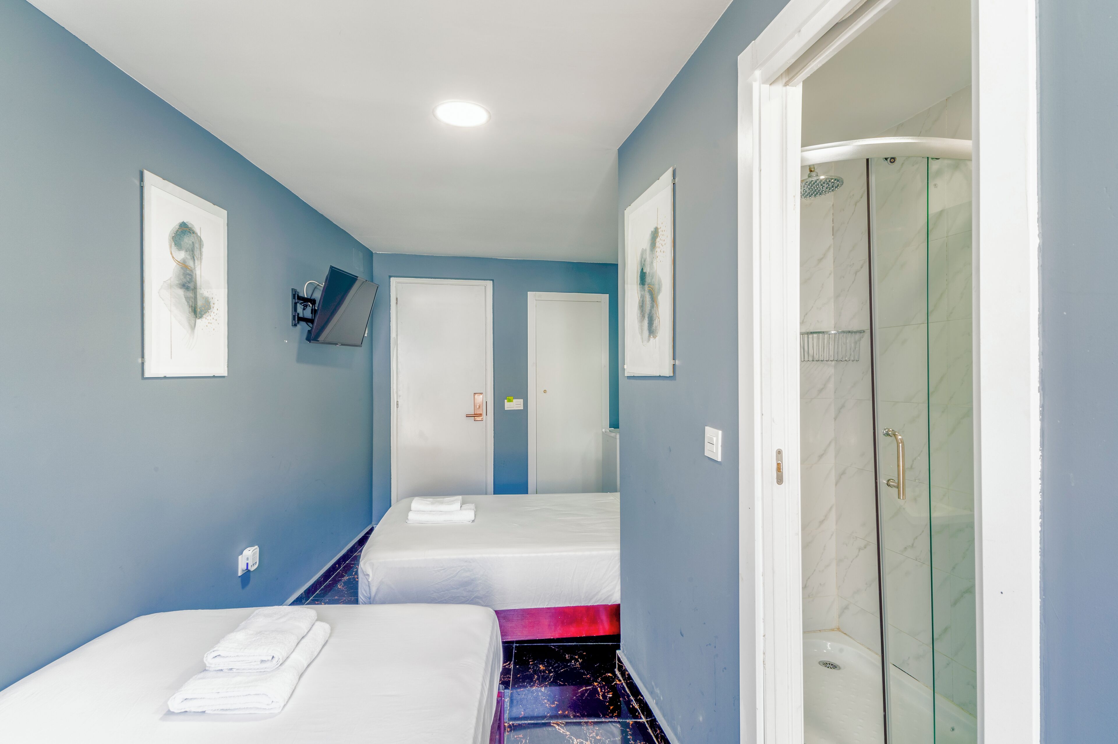 A hotel room with two beds, a shower, and artwork on the walls.