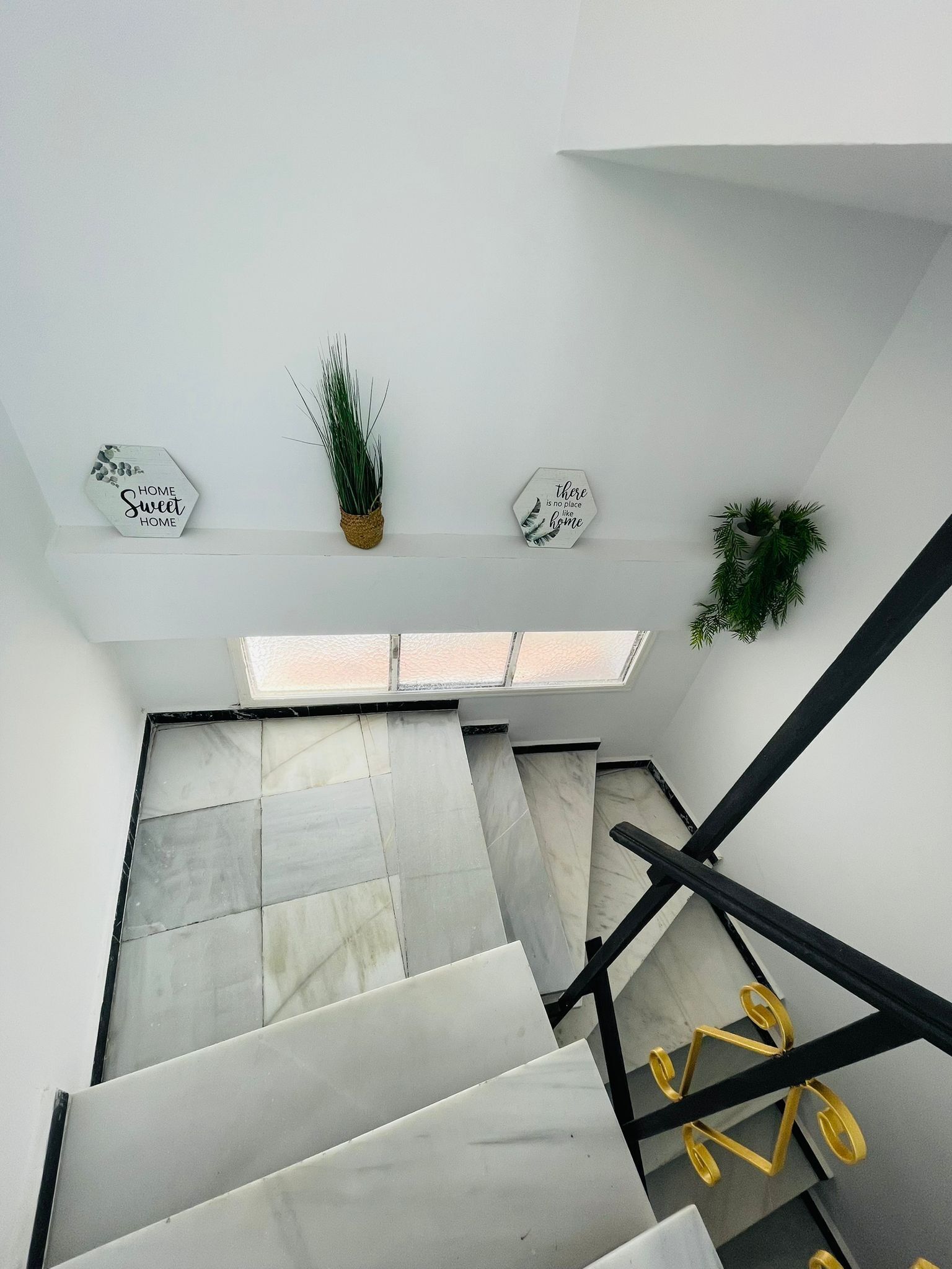 Una escalera moderna con tragaluces, paredes blancas y señalizaciones hexagonales decorativas.