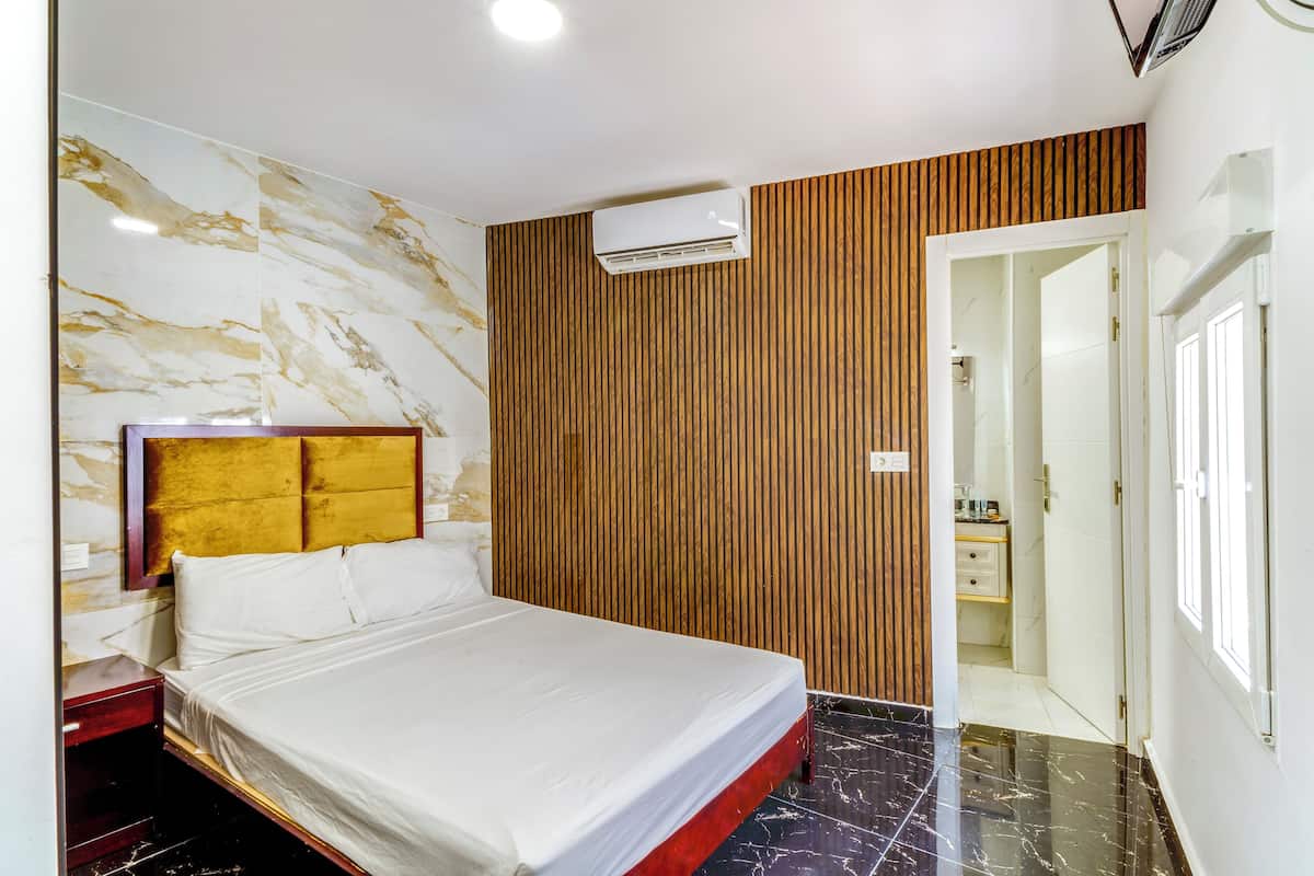 Een hotelkamer met een bed, houten paneelwand, marmeren wand en een airconditioner.