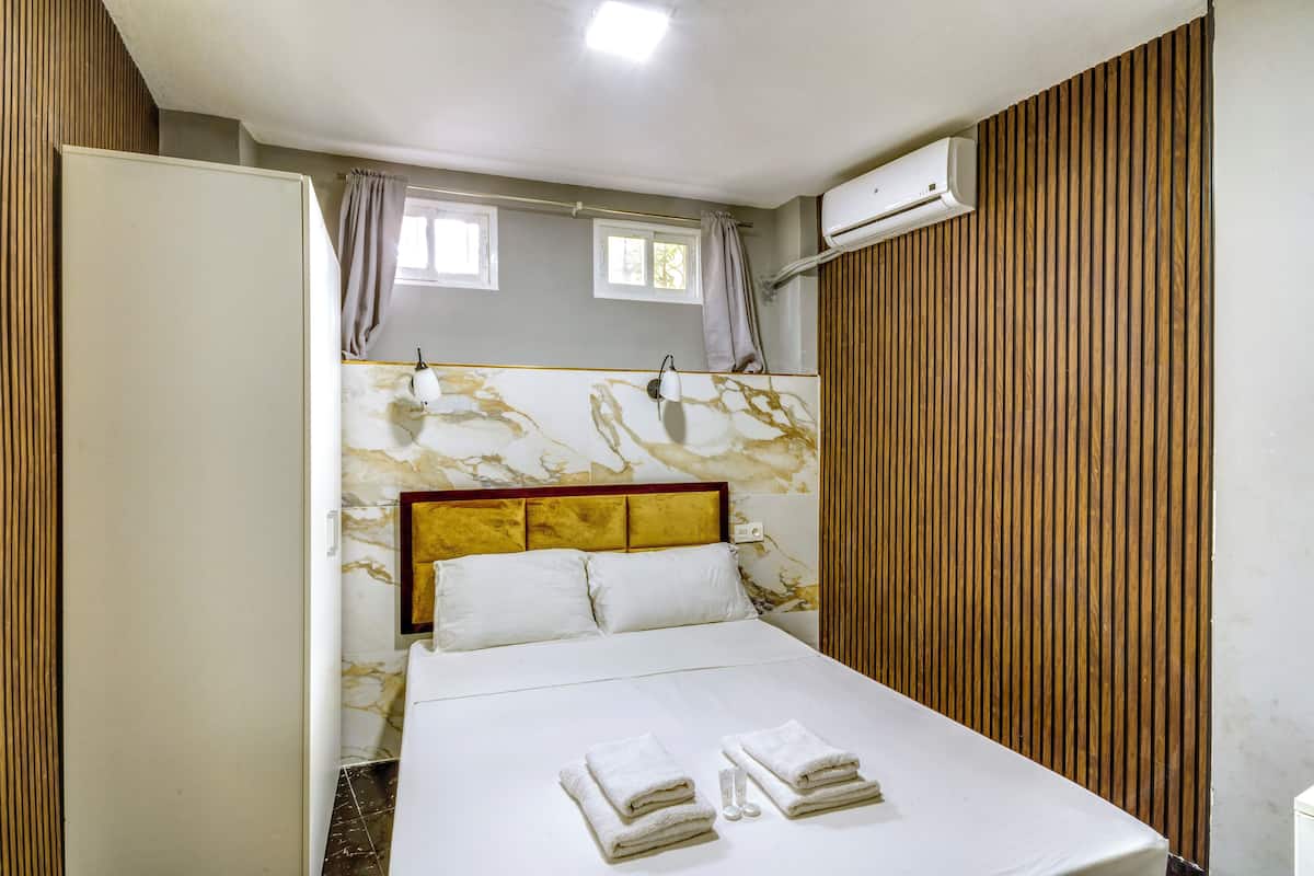 Een keurig opgemaakt bed met witte lakens en handdoeken, een hoofdeinde met een marmerpatroon en een wand van houten panelen.