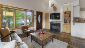 A modern living room with a fireplace, a mounted deer head, and a kitchen area with wooden cabinets and a TV. - Private Sauna, Hot Springs Close, Monthly Discount (Durango)