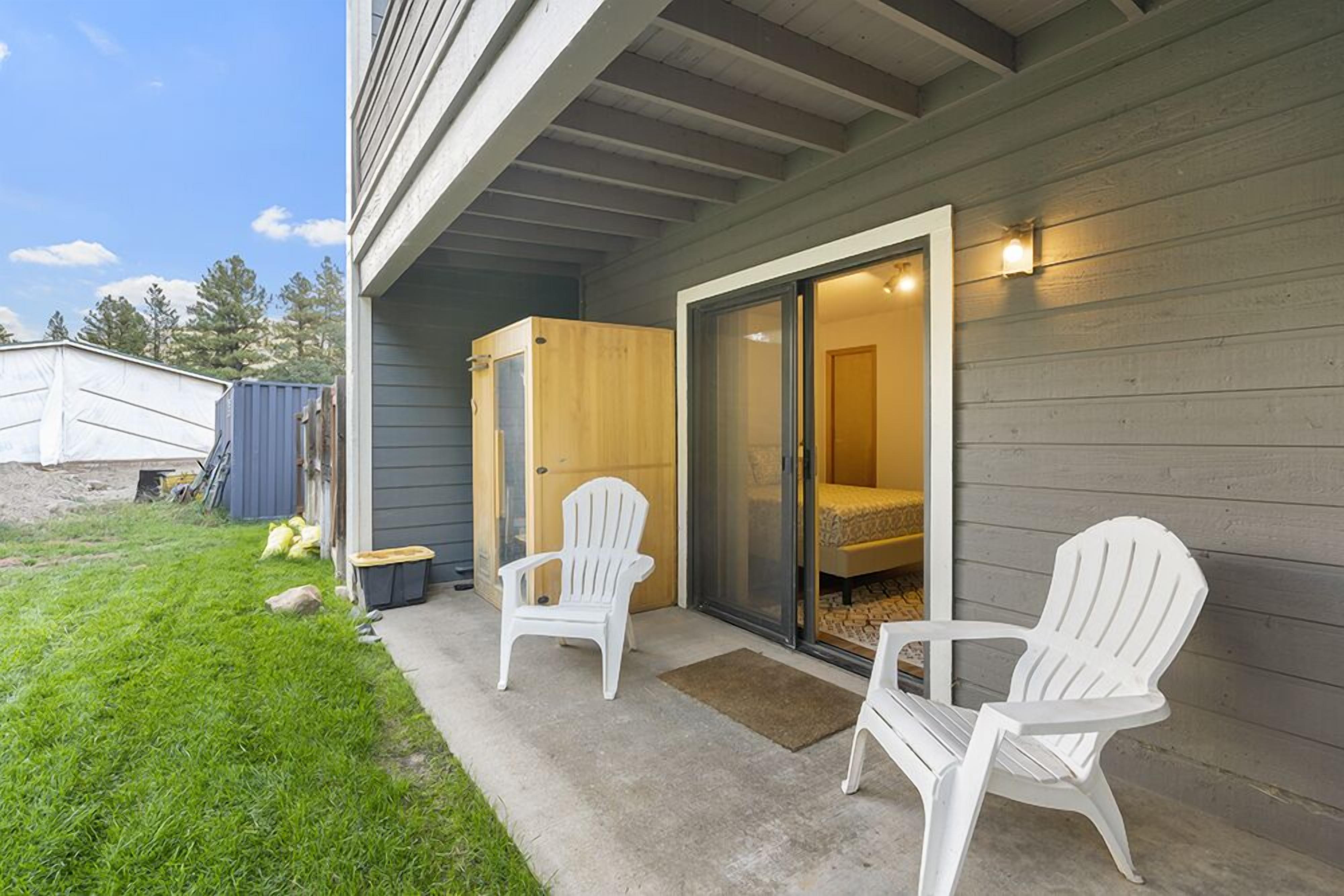 A covered patio with two Adirondack chairs, a sliding glass door leading to a bedroom, and a small outdoor area with a shed and bags.