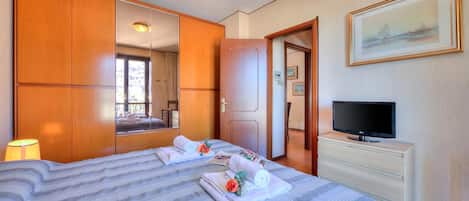 A hotel room with a bed, a TV, a dresser, a mirror, and a painting on the wall.