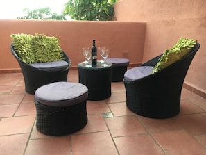 A patio area with wicker furniture, including two chairs and a round table, with a bottle and glasses on the table.